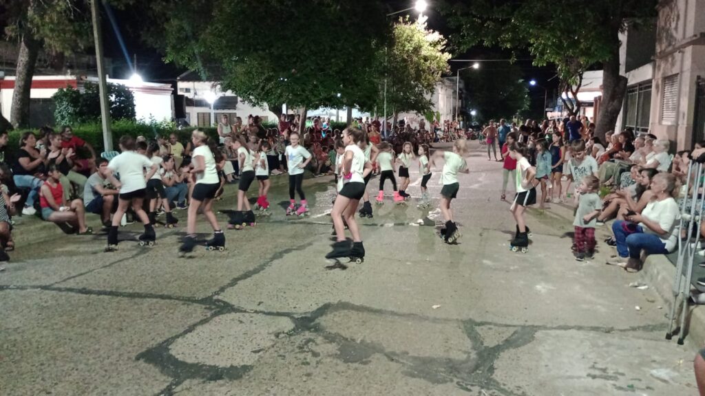 Jóvenes bailando y patinando de noche en una calle ante gran cantidad de público observando.