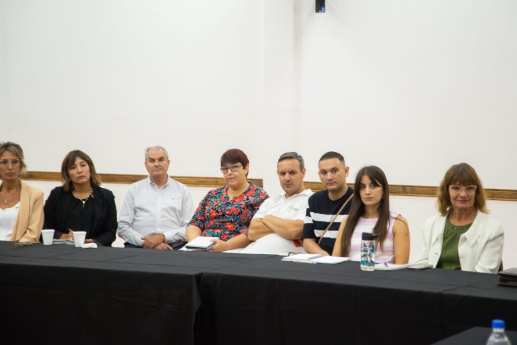 varias personas sentadas a una mesa larga ocn mantel negro escuhando, entre ellas, la Directora de Turismo de Concepciòn del Uruguay Laura Saad.
